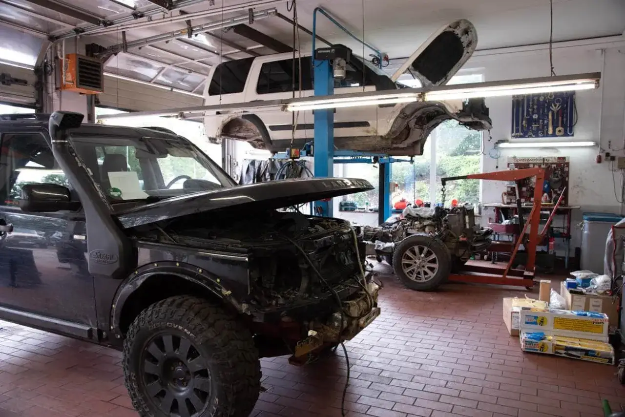 Werkstatt mit zwei Land Rover Discovery 4. Einer vorne mit ge&ouml;ffneter Haube, der andere auf der Hebeb&uuml;hne. M&ouml;gliche Schwachstellen werden hier behoben.