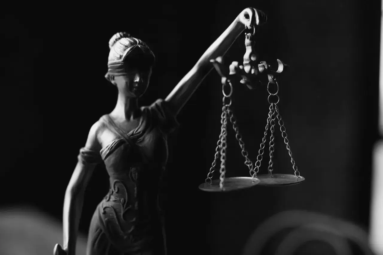 Figurka Temidy z wagą, symbol sprawiedliwości. Ciemne tło podkreśla jej powagę, niczym kruk komornik czuwający nad prawem.