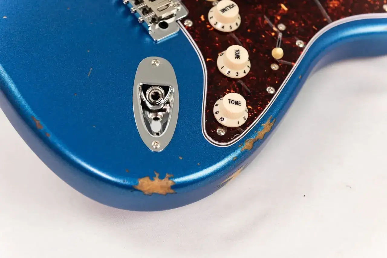 Guitare &eacute;lectrique bleue avec un aspect vieilli, montrant des &eacute;clats de peinture r&eacute;v&eacute;lant le bois. Le **relicage guitare** lui donne un charme vintage.