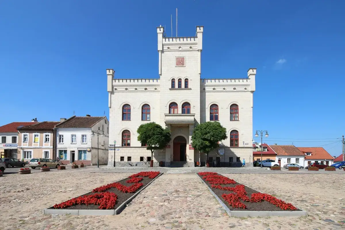 Ratusz w Pasym – serce miasta i jego główne atrakcje. Brukowany rynek z czerwonymi rabatami kwiatowymi.