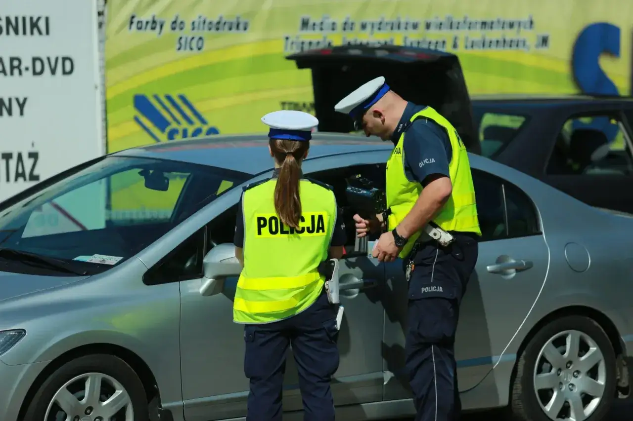 Dwóch policjantów w kamizelkach odblaskowych przy srebrnym samochodzie. Czy policja może wejść na teren prywatny bez nakazu?