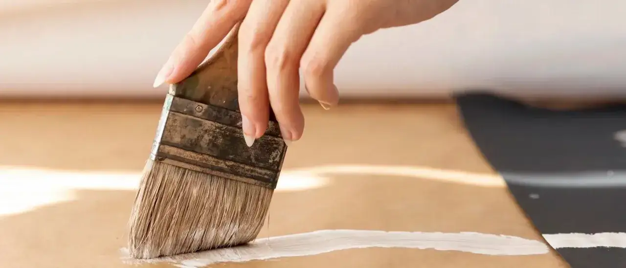 Main d'une personne peignant une surface en MDF avec un pinceau et de la peinture blanche.