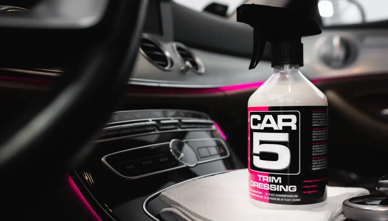 En flaska CAR5 Trim Dressing står på en mikrofiberduk i en bilinteriör med rosa ambientbelysning. En perfekt concept vista för bilvård.