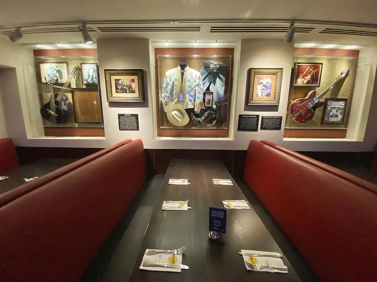 Wystrój Hard Rock Cafe z pamiątkami muzycznymi: gitary, stroje, kapelusz. Czerwone ławki i stoły z nakryciami.