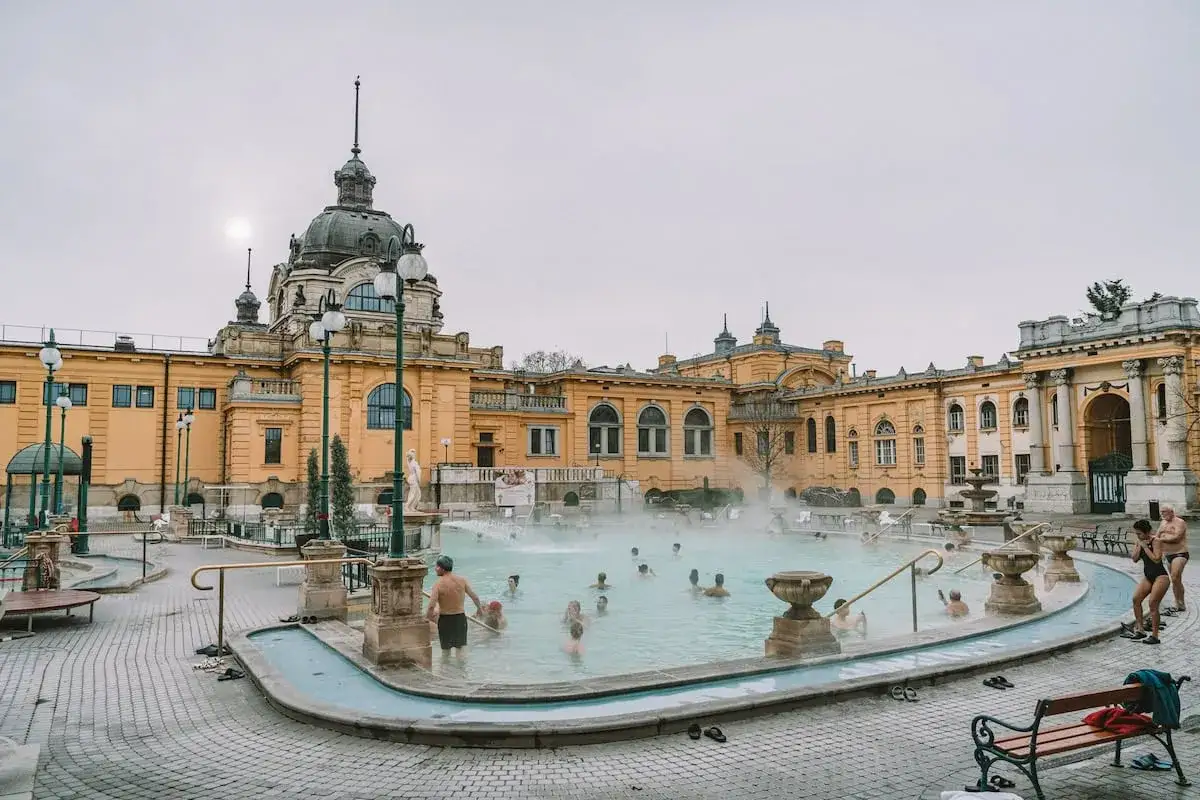 Menschen entspannen im dampfenden Wasser eines Budapester Thermalbads vor pr&auml;chtiger Architektur.
