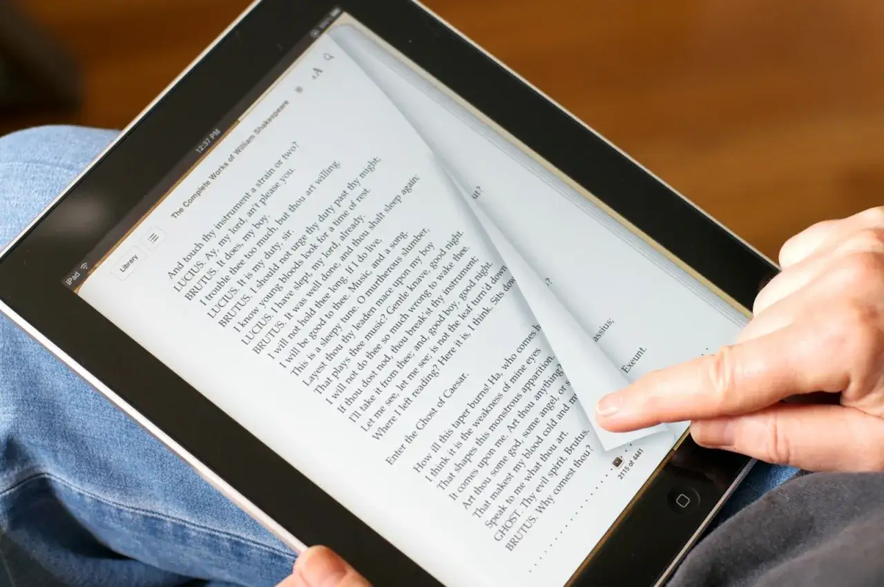 Comment lire un ebook : une main tourne une page sur une tablette affichant les &oelig;uvres compl&egrave;tes de Shakespeare.