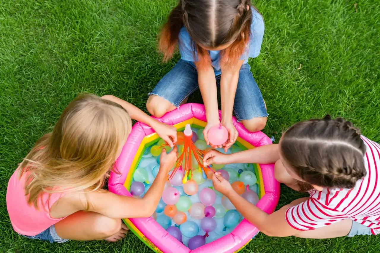 Bambine giocano con palloncini d'acqua in una piscina gonfiabile, perfetti giochi per l'estate.