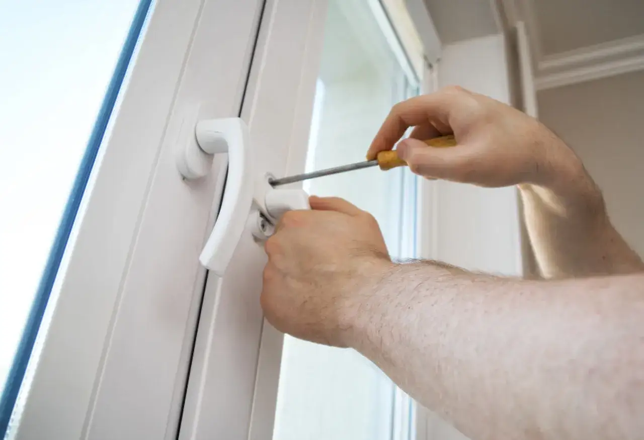 Main tenant utilise un tournevis pour changer la poignée d'une fenêtre en aluminium.