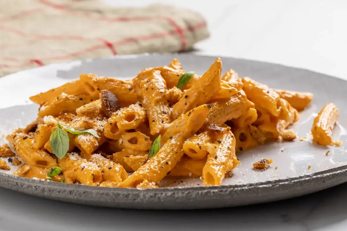 Penne cremose con salsa ai peperoni, guarnite con basilico fresco e crostini croccanti. Un piatto invitante e saporito.