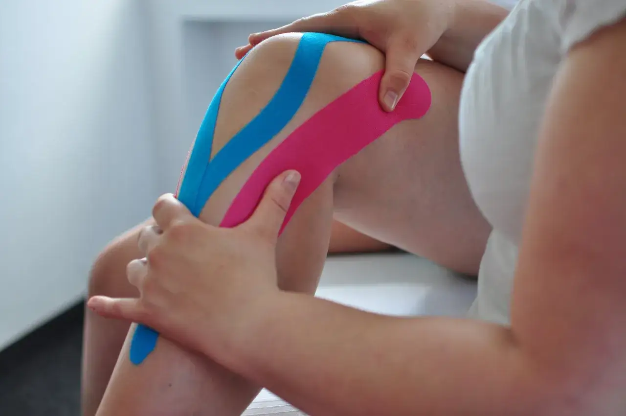Kolano skoczka z kolorowymi plastrami kinezjotapingowymi, wspierającymi mięśnie i stawy.