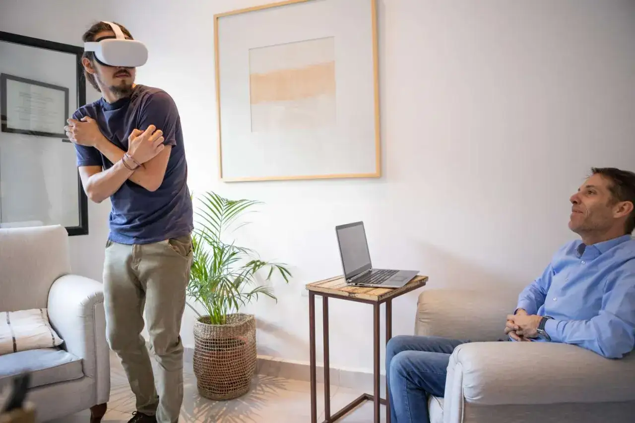 Mężczyzna w goglach VR przeżywa lęk wysokości, jakby brał tabletki na lęk wysokości. Obok siedzi terapeuta.