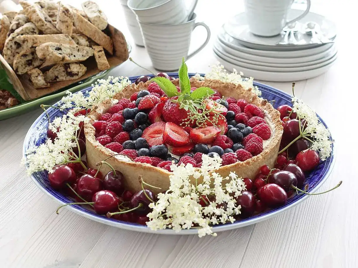 En Ernst-inspirerad bärpaj med jordgubbar, hallon och blåbär, dekorerad med körsbär och fläderblommor. Perfekt för sommaren!