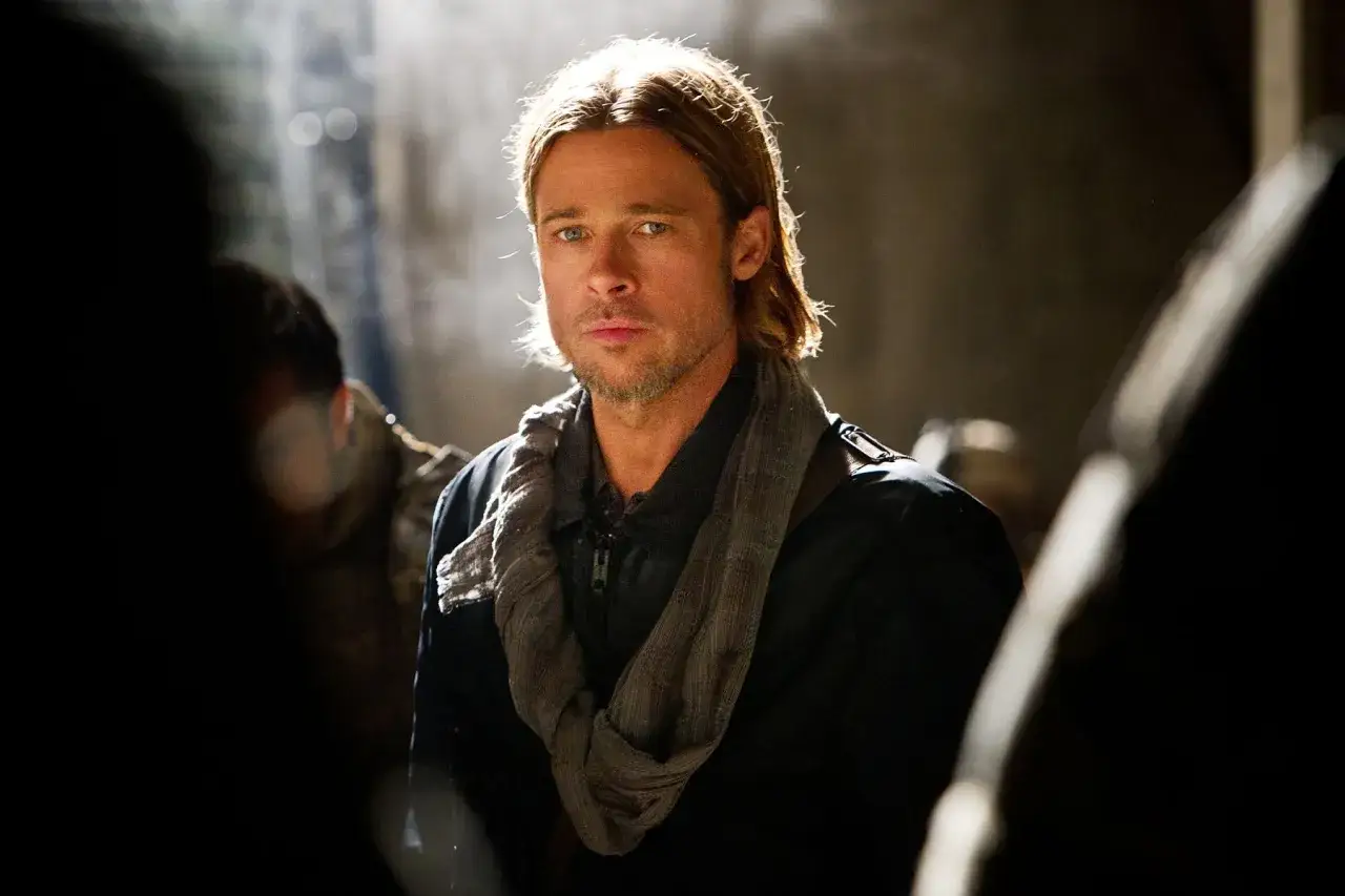 Brad Pitt jako Gerry Lane w filmie World War Z, zamyślony, w ciemnej kurtce i szaliku, w otoczeniu innych postaci.