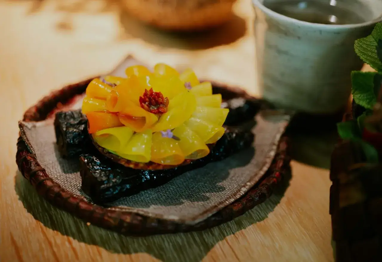 En konstnärlig dessert med gula och orangea blad, som en blomma, serverad på en mörk bas. En upplevelse från en michelin restaurang sverige.