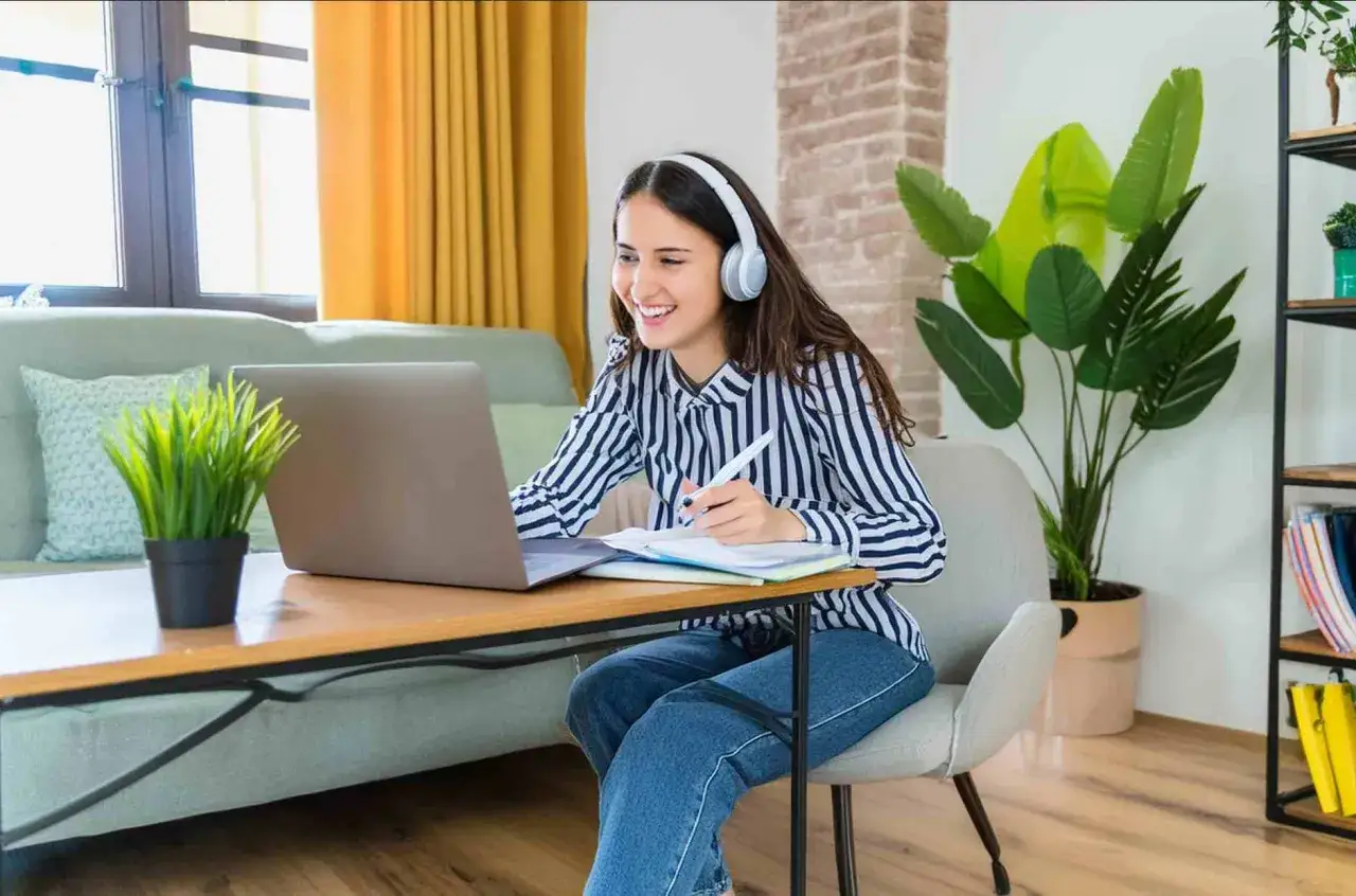 Studentessa sorridente studia da casa con cuffie e laptop, un'esperienza di apprendimento flessibile come quella offerta dall'università Pegaso.