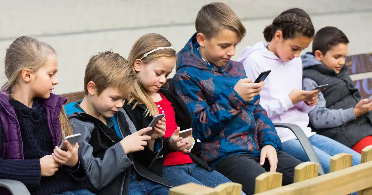 Dzieci siedzą na ławce, każde wpatrzone w sw&oacute;j smartfon. Czy to efekt wertera, co to znaczy dla ich relacji?