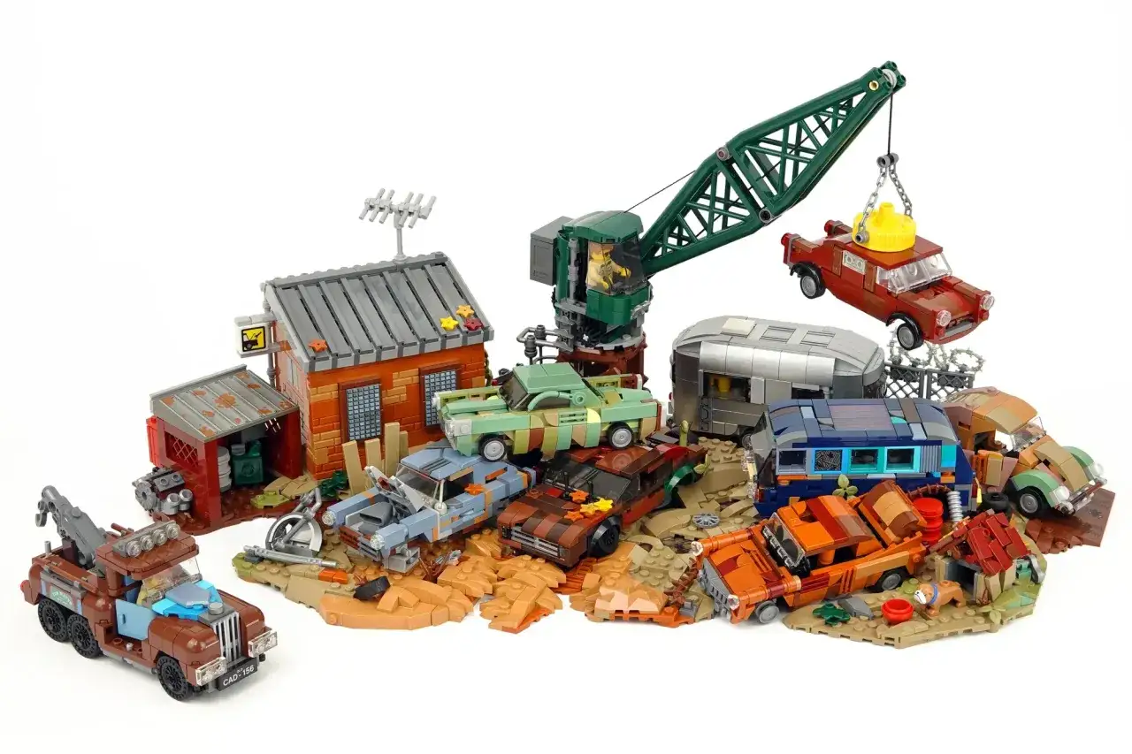 Ein detailreicher **Lego Schrottplatz** mit einem Kran, der ein Auto hebt, verschiedenen verrosteten Fahrzeugen, einem Wohnwagen und einem kleinen Geb&auml;ude.