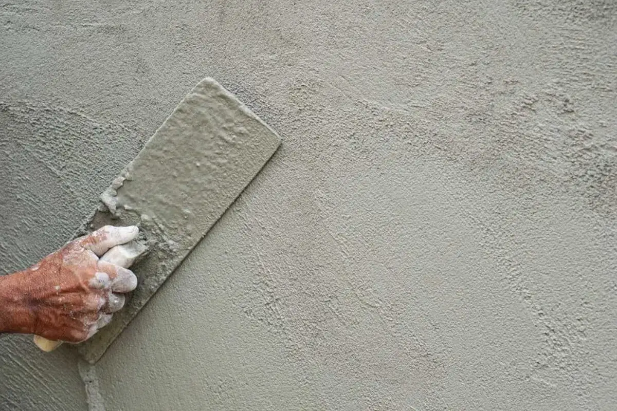 Mano aplicando enfoscado de cemento con llana, creando una textura rugosa y uniforme en la pared.