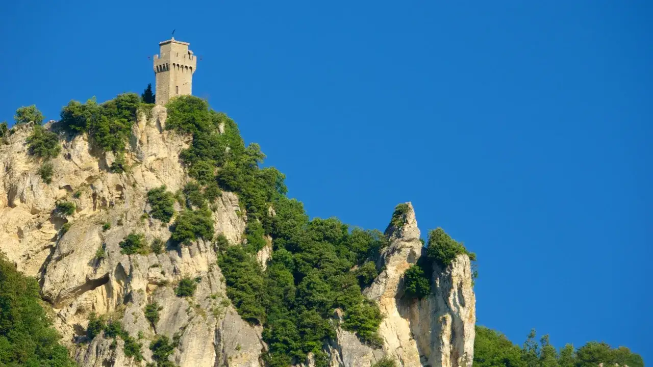 Torre medievale su una roccia scoscesa, parte del **San Marino castle**, con vegetazione rigogliosa e cielo azzurro.