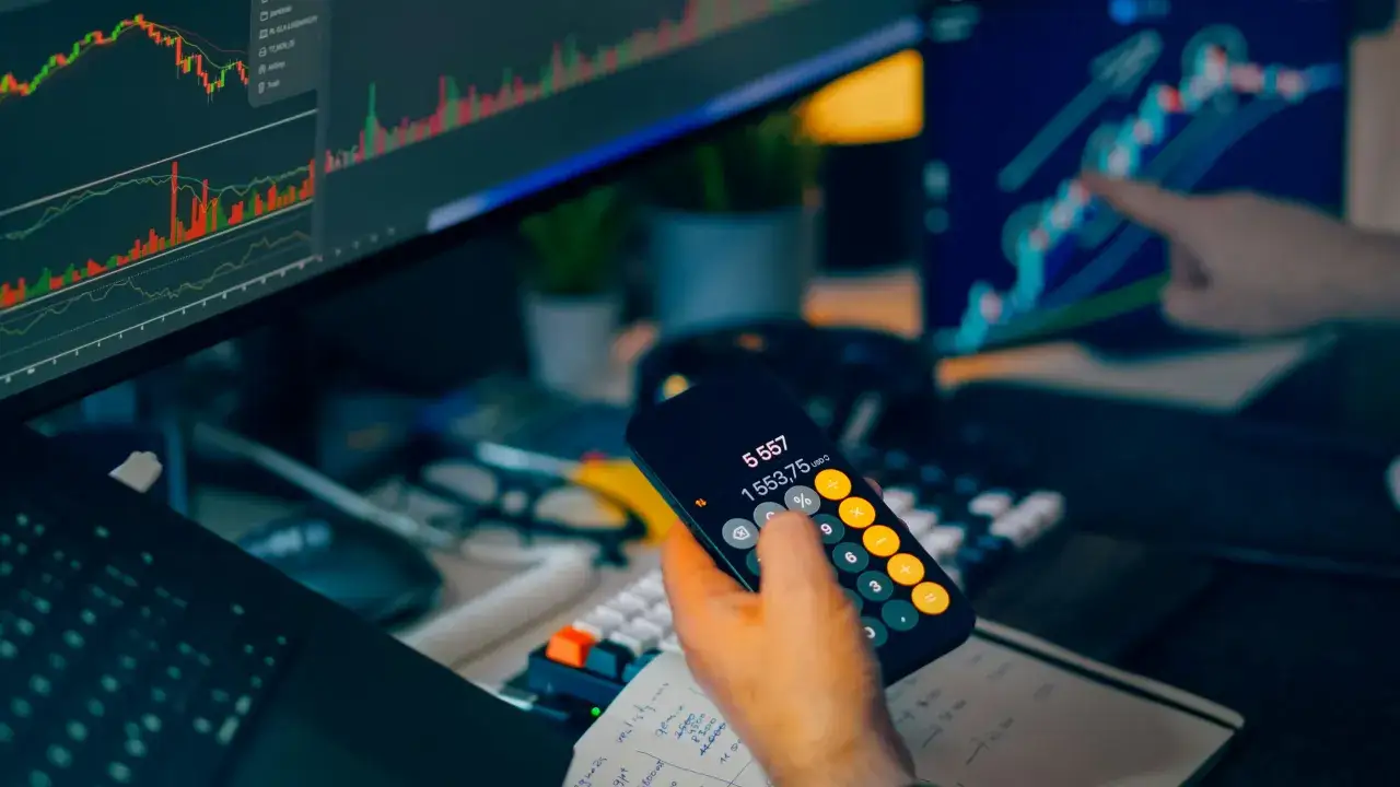 Operador de scalping trading revisa gráficos en pantalla y calcula ganancias en su móvil.