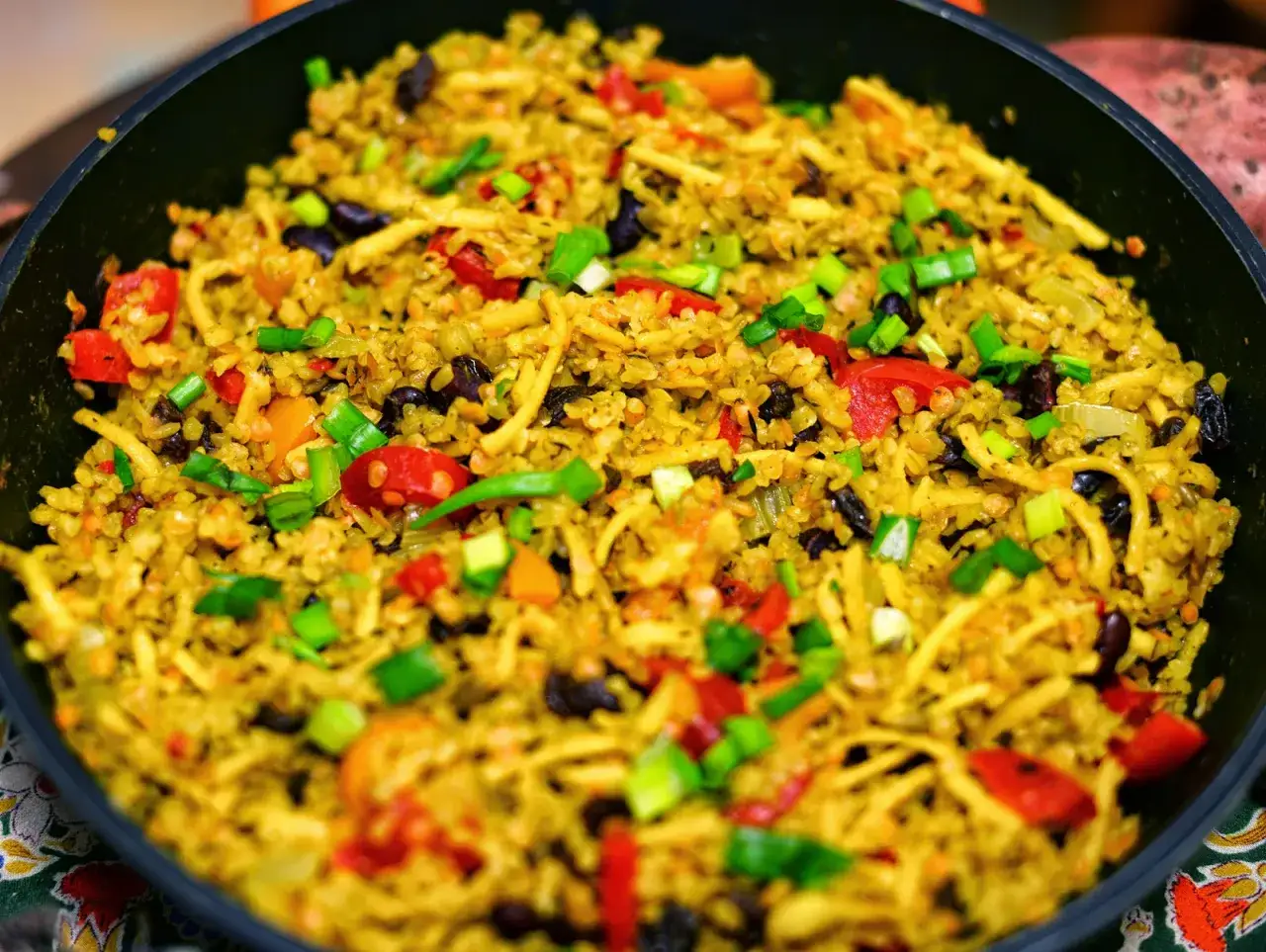 Kolorowe danie z kaszą bulgur, fasolą, papryką i szczypiorkiem w czarnej patelni.
