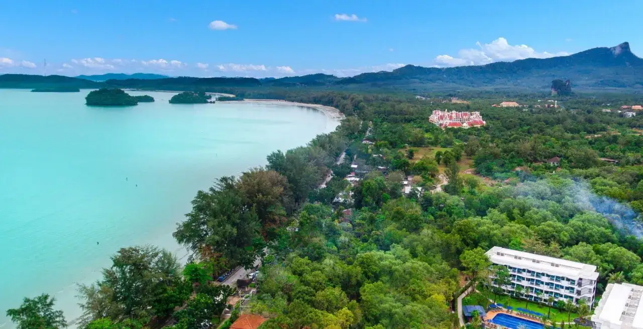 Widok na Ao Nang Beach z turkusową wodą, zielonymi wyspami i górami w tle. Widać hotele i bujną roślinność.