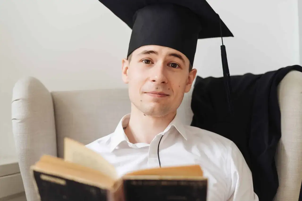 Diplômé en intelligence artificielle, un jeune homme en toque et robe de cérémonie lit un livre ancien, prêt à explorer de nouveaux horizons.