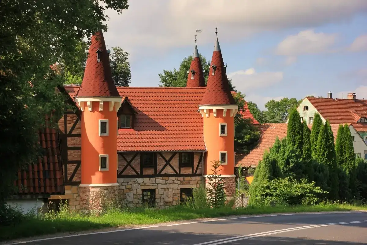 Pomarańczowy zamek śląskich legend z czerwonymi stożkowymi dachami, kamienną podstawą i drewnianymi belkami.