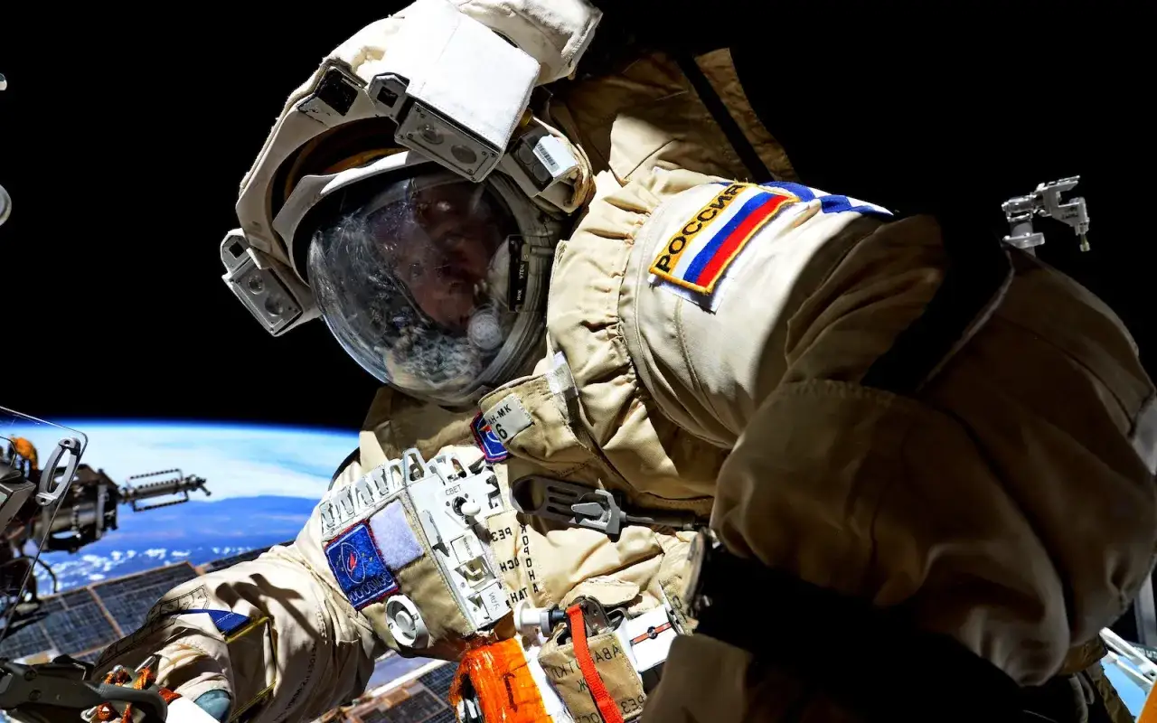 Astronaut w skafandrze kosmicznym z flagą Rosji na ramieniu, unoszący się nad Ziemią.