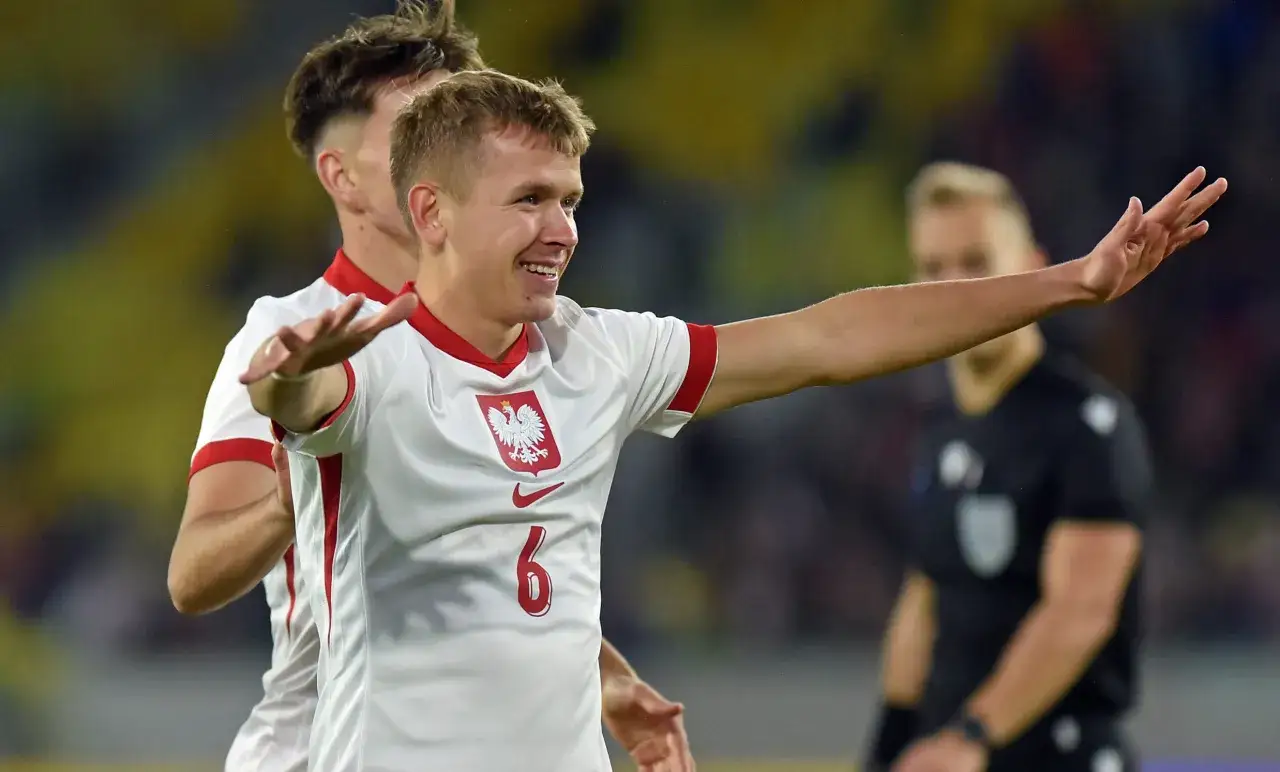 Piłkarz w białej koszulce z orłem na piersi cieszy się po golu. Radość po bramce w eliminacjach Euro: rozgrywki.