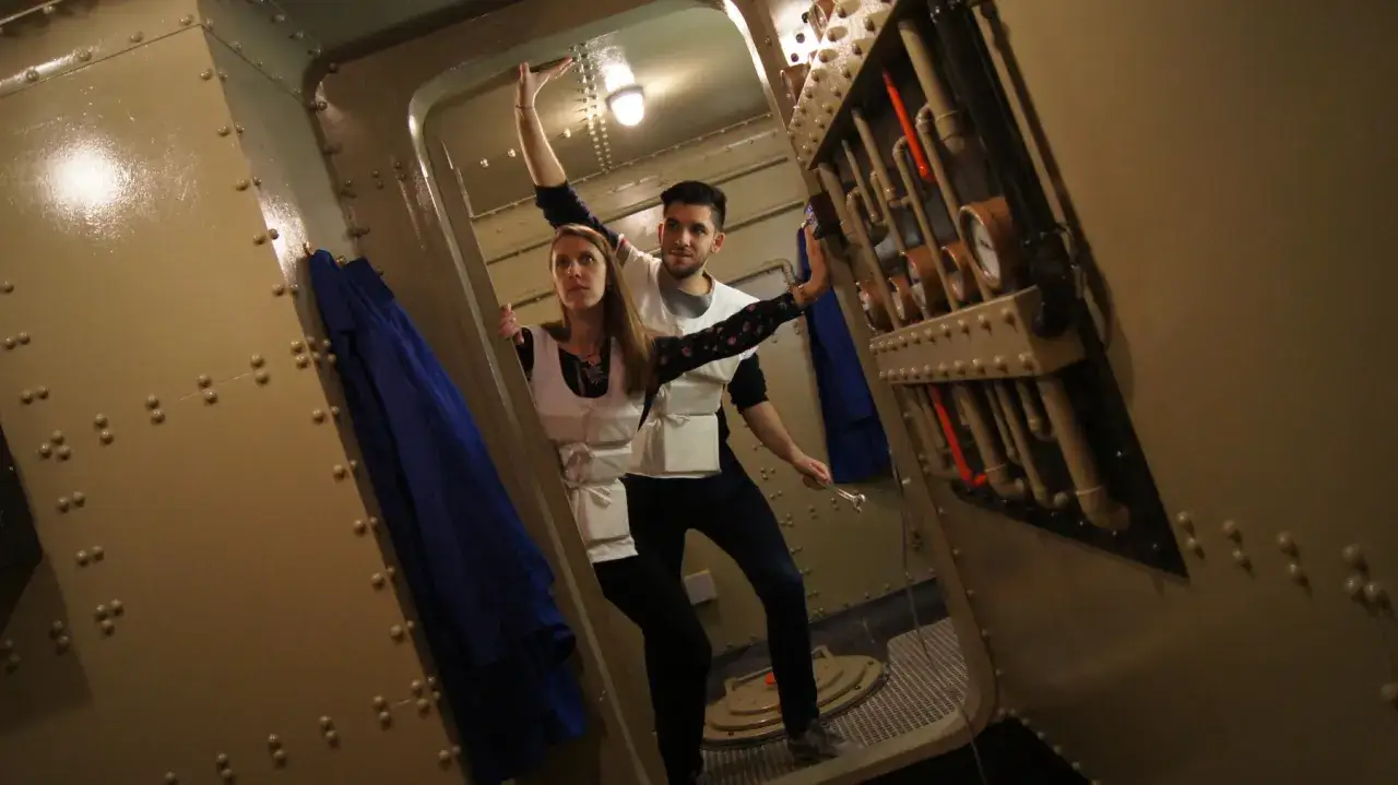 Un couple s'amuse dans un **escape game insolite &agrave; Paris**, explorant un d&eacute;cor de sous-marin avec des instruments et des tuyaux.