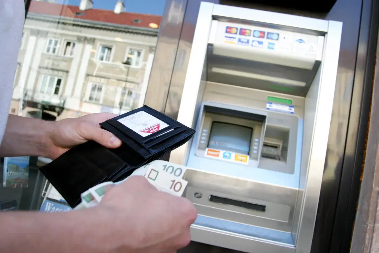 Ręka z portfelem i banknotami 100 i 10 zł przy bankomacie. Szybka transakcja w zen wpłatomacie.