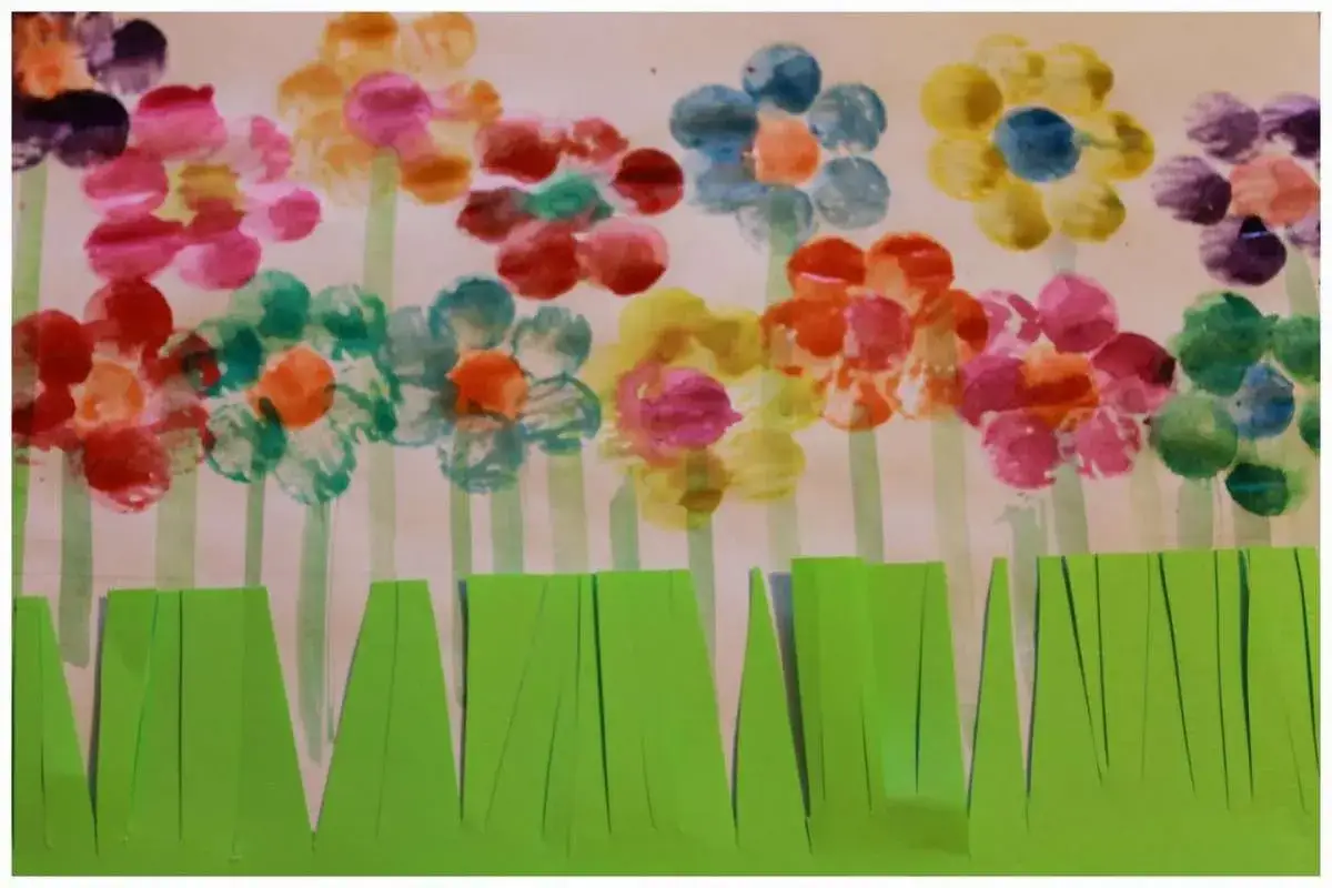Fiori colorati con impronte di dita, un esempio di frasi sul riciclo creativo per bambini. L'erba &egrave; fatta di carta verde tagliata.
