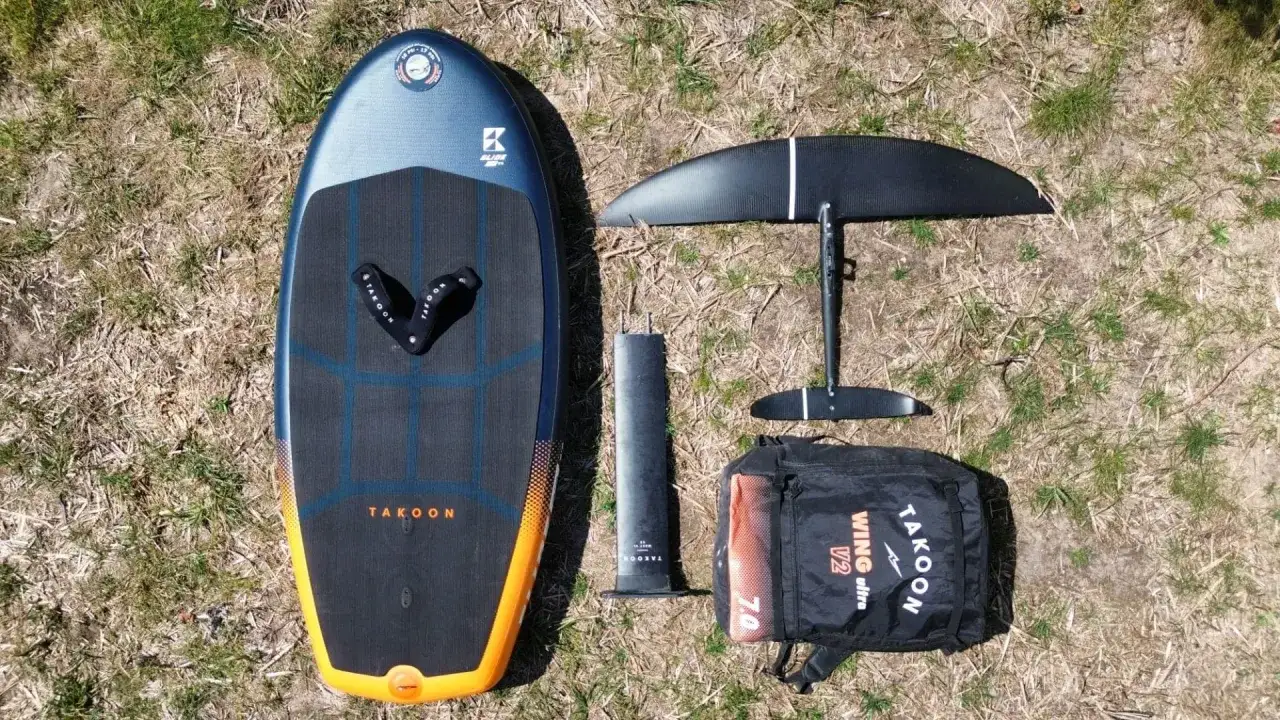 Takoon Wing Foil Board, Mast, Flügel und Tasche liegen auf trockenem Gras bereit für das Wing surfen.