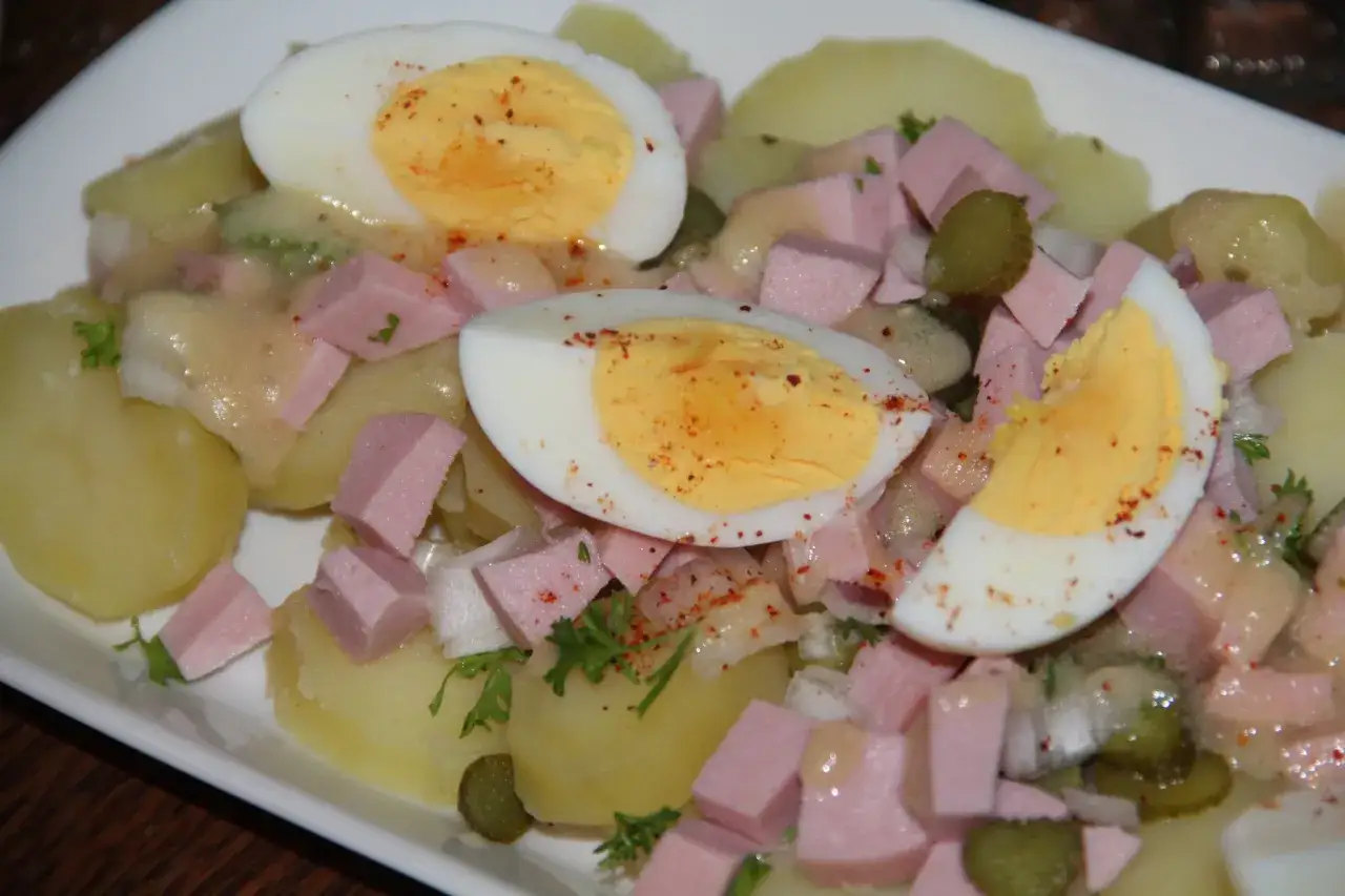 Salade de pomme de terre avec &oelig;ufs durs, jambon en d&eacute;s, cornichons et persil. Un plat r&eacute;confortant et savoureux.