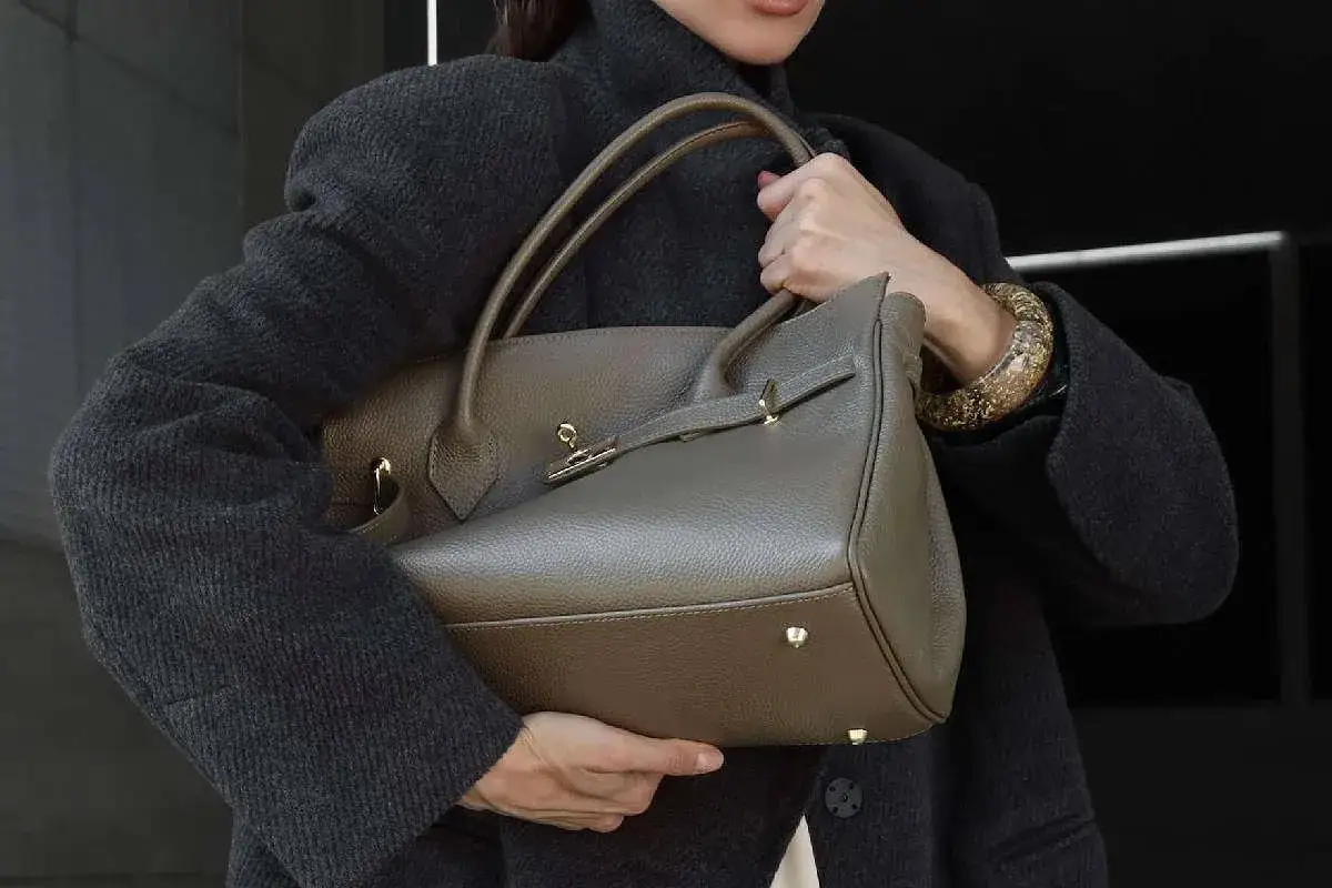Elegancka, szara torebka damska premium z brązowymi rączkami, noszona przez kobietę w płaszczu.