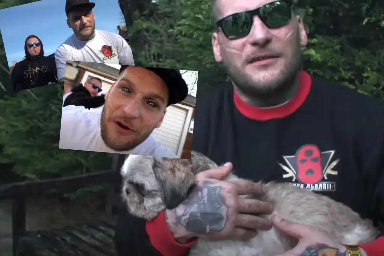 Mężczyzna z bliznami na twarzy i tatuażami trzyma psa. Na koszulce widnieje logo