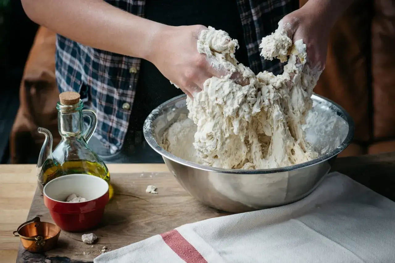 Händer som knådar deg i en skål. Ingredienser för pizzadeg recept syns, som olja och jäst.