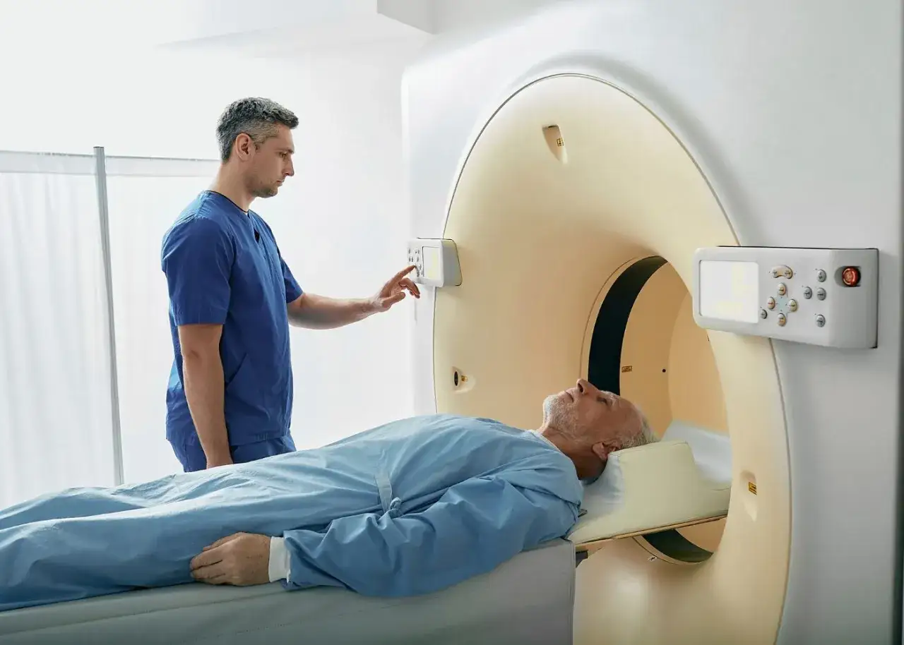 Pacjent leży na stole tomografu, technik przygotowuje badanie. Czy można pić wodę przed tomografią z kontrastem? Zapytaj lekarza.