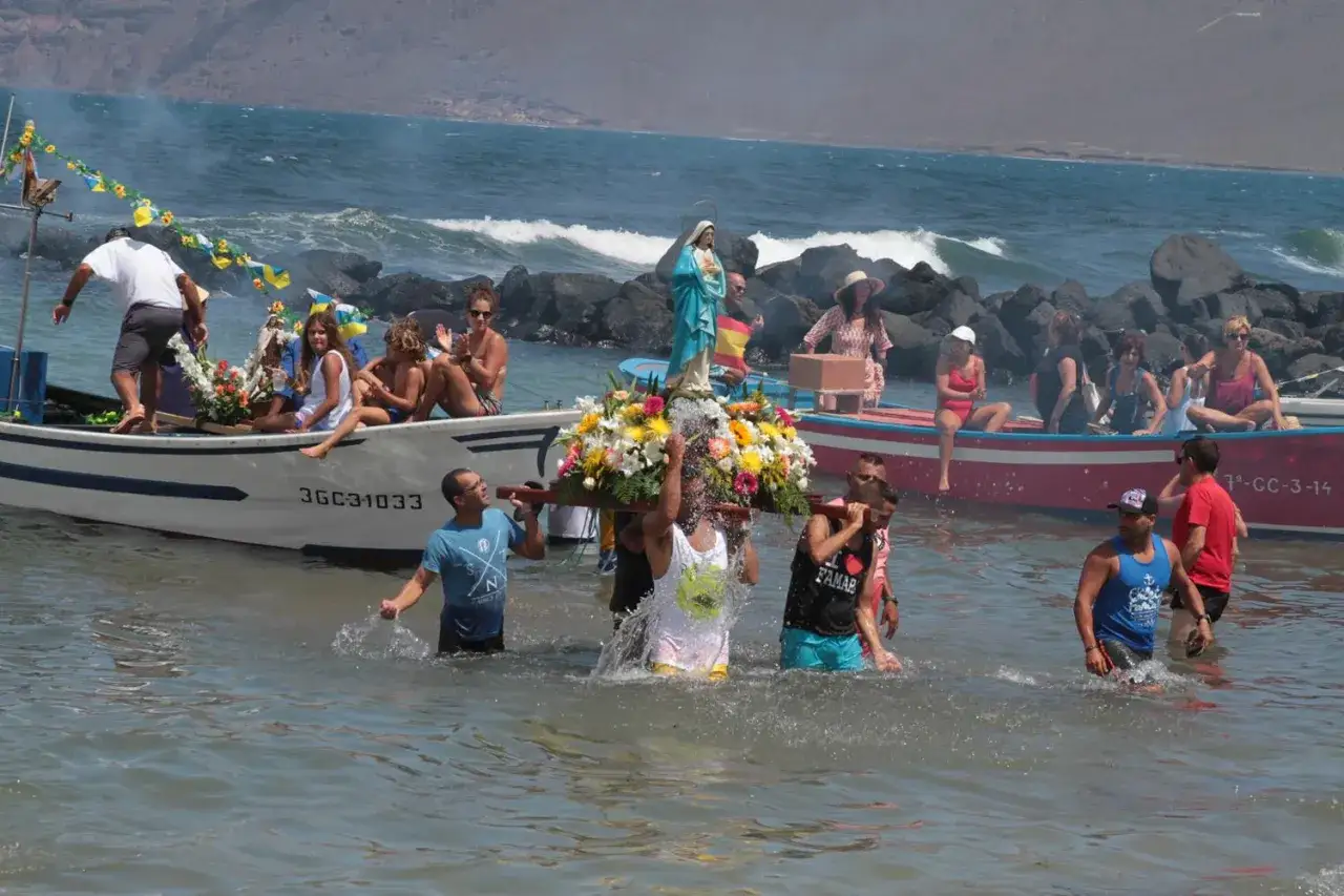 Procesión marítima en España con una imagen de la Virgen, flores y gente en el agua.