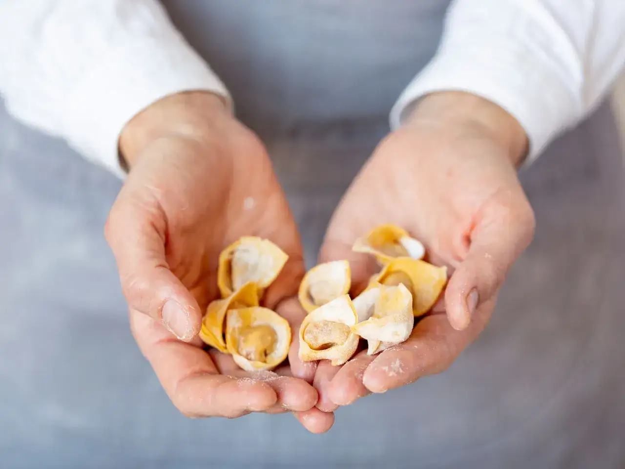 H&auml;nde halten frisch gemachte, kleine Tortellini. Das Ergebnis von liebevollem **Tortellini selber machen**.