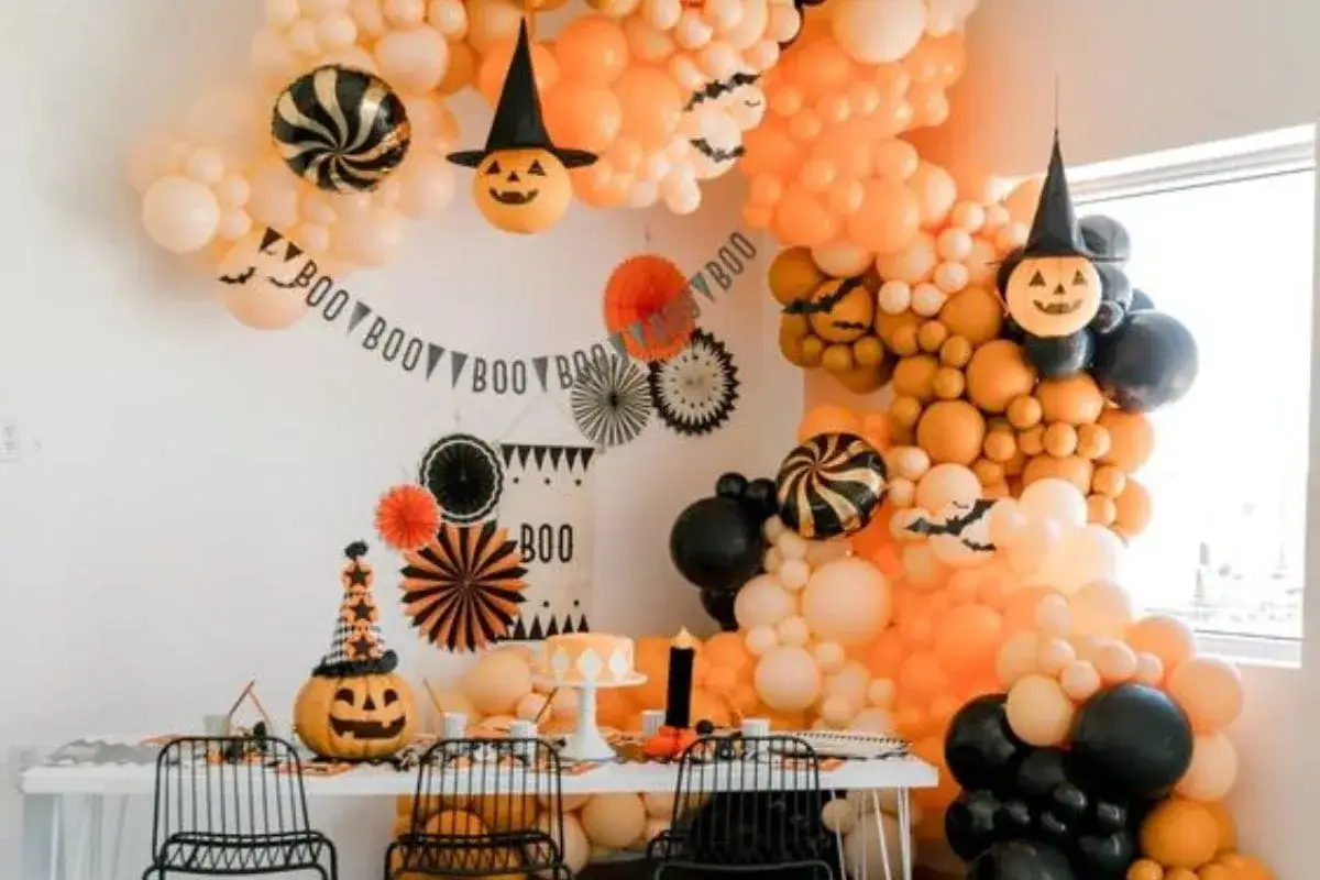 Un tavolo addobbato per Halloween con palloncini arancioni, neri e bianchi, zucche intagliate e festoni con le parole di Halloween 