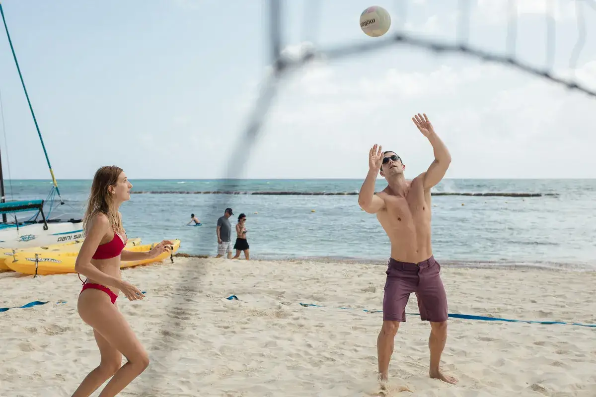 Jóvenes disfrutan de juegos en la playa, jugando voleibol bajo el sol.