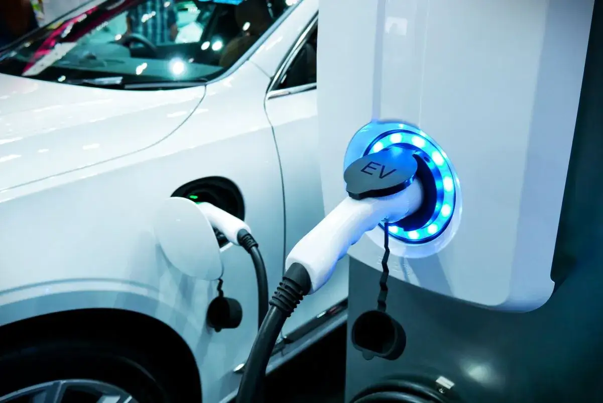 Ładowanie samochodu elektrycznego w domu: białe auto podłączone do stacji ładowania EV z niebieskim podświetleniem.