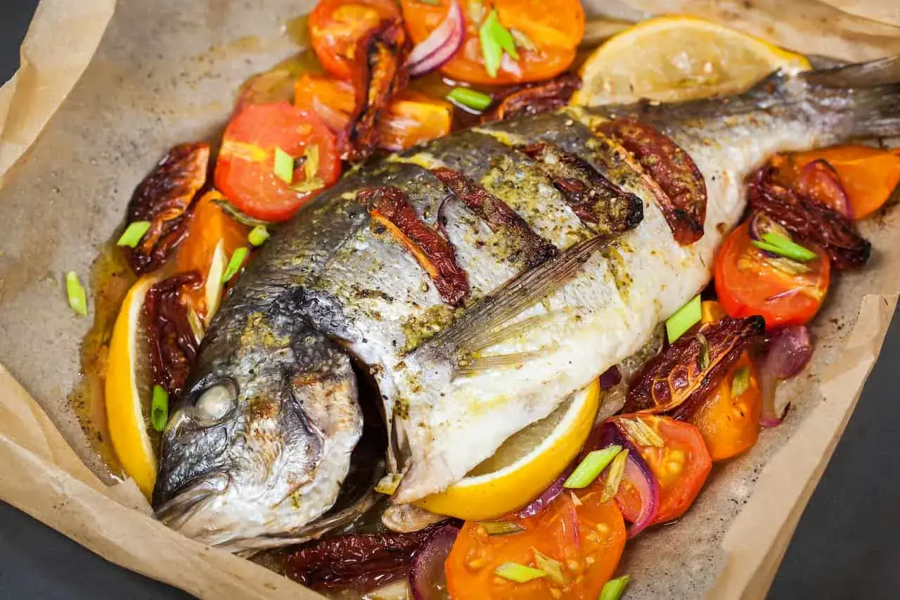 Dorada a la gallega recién horneada, con rodajas de tomate, limón y cebolla morada, todo envuelto en papel de horno.