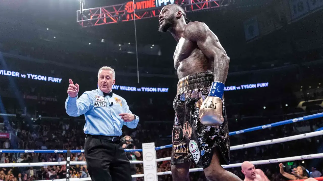 Deontay Wilder, in his flashy shorts, faces the referee who signals a command. Boxing terms like
