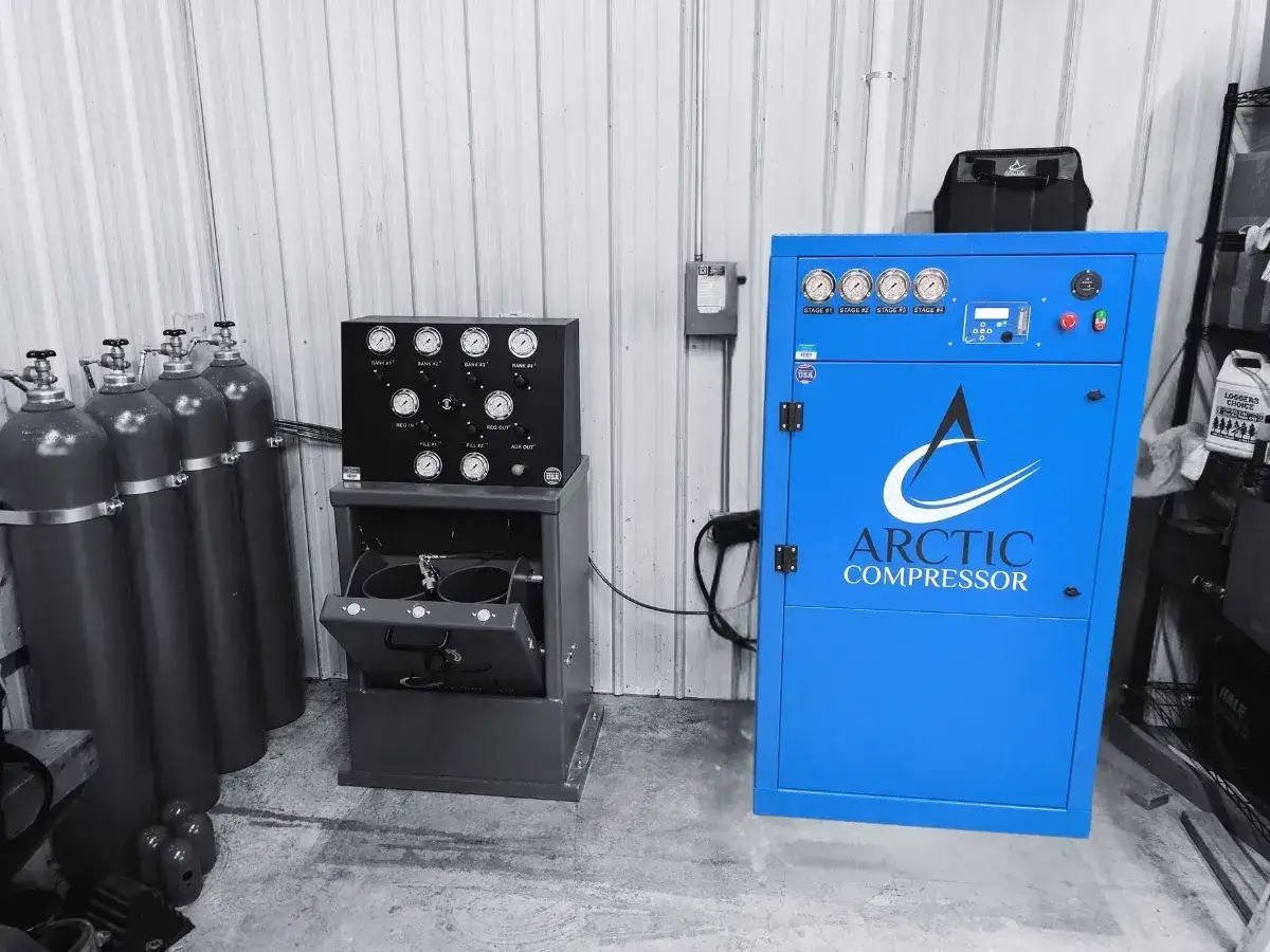 Un compresor de aire respirable Arctic Compressor azul junto a cilindros de gas y un panel de control.