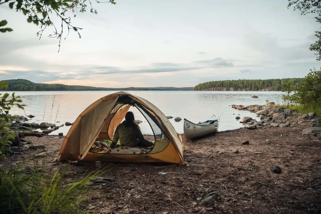Ein Zelt am Seeufer, daneben ein Kanu. Hier darf man in Schweden wildcampen und die Natur genie&szlig;en.