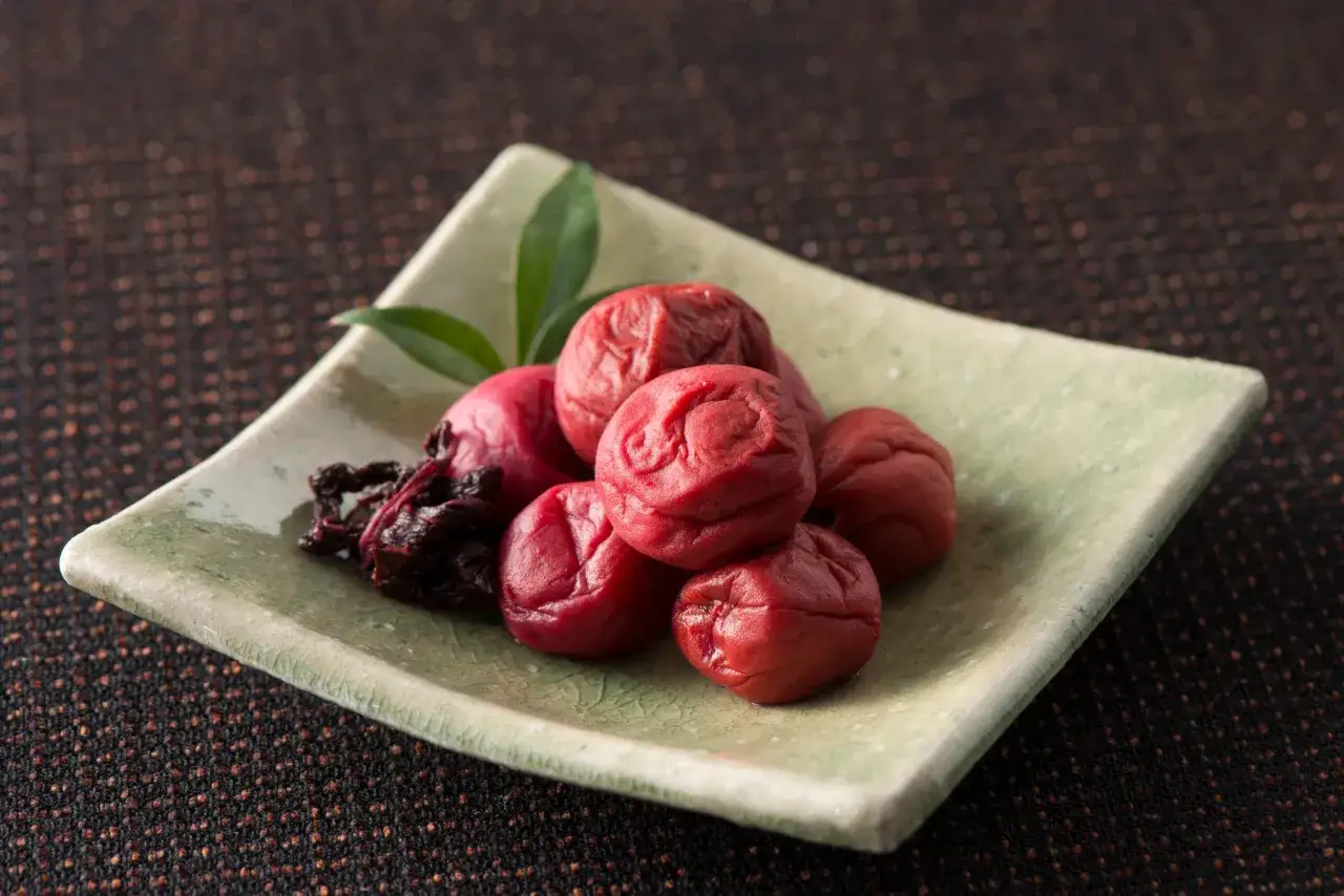 Umeboshi, prugne salate e fermentate, servite su un piatto verde chiaro. Scopri i benefici degli umeboshi per la tua salute.