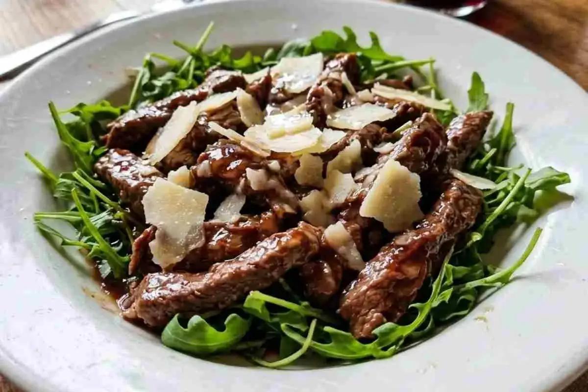Straccetti di manzo succulenti su letto di rucola fresca, guarniti con scaglie di parmigiano. Un piatto invitante e saporito.